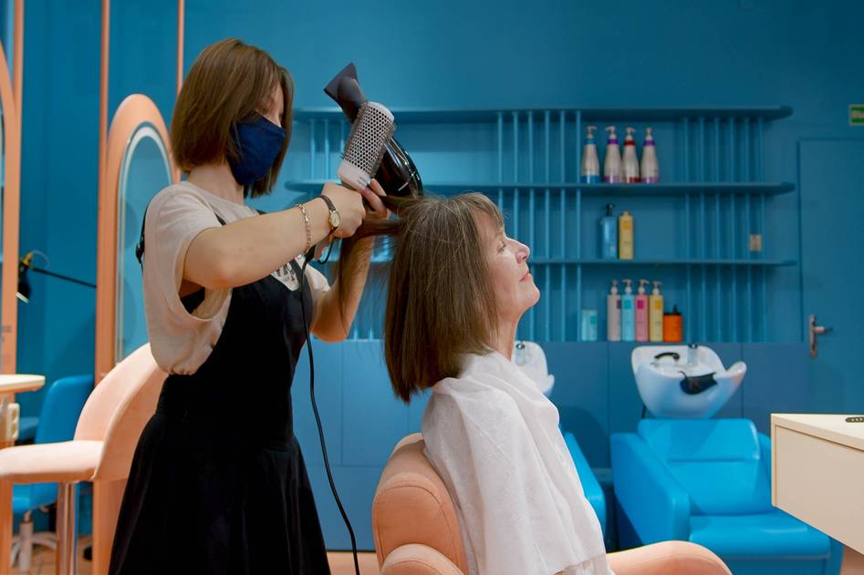 Close-up of glossy, healthy hair with a hand holding a hair conditioner bottle against a soft-focus bathroom background